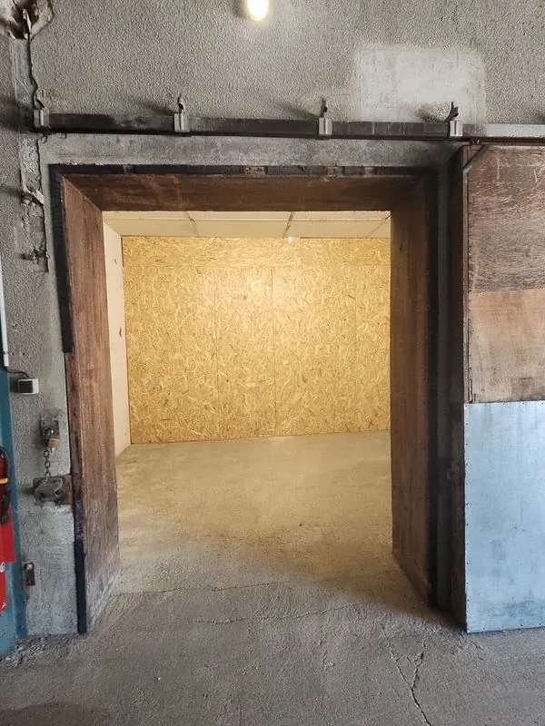 Entrée d’un box fermé par une porte métallique, avec cloison en bois au fond
